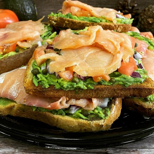 Avocado toast with smoked salmon, diced tomatoes, red onion, and capers on a black plate.