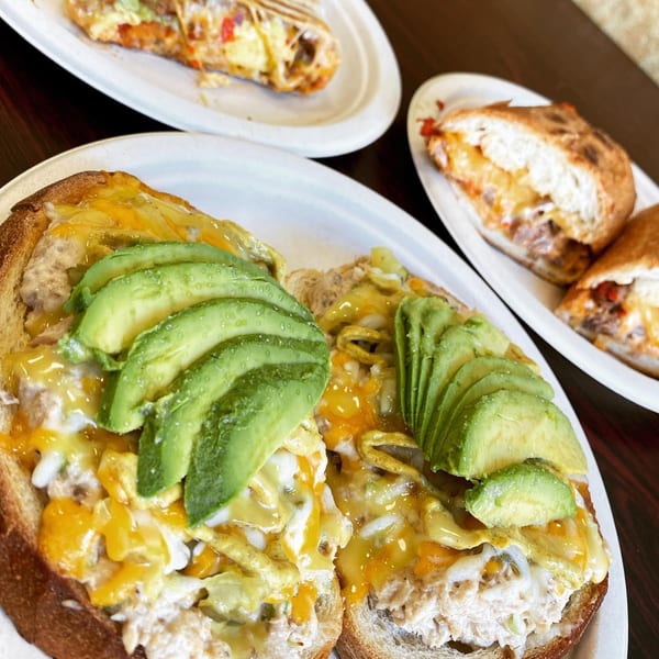 Avocado Toast with melted cheese and egg, alongside breakfast burritos on white plates.