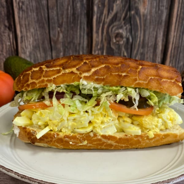 Egg salad sub sandwich with lettuce and tomato on a white plate with a wooden background.