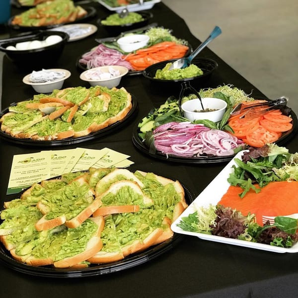 A catering spread of avocado toast, smoked salmon, and various toppings on a black tablecloth.