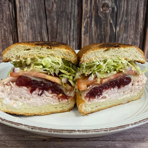 A turkey sandwich with cranberry sauce, lettuce, tomato, and onion, cut in half on a white plate.
