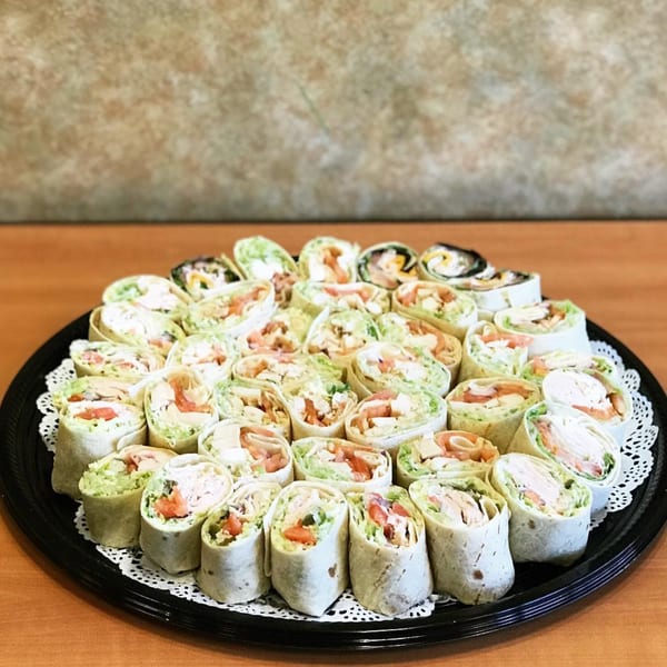 A black platter filled with numerous tortilla pinwheel wraps, showcasing various fillings like avocado, chicken, and tomato.