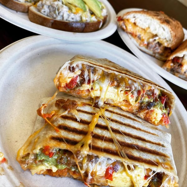 Cheesy breakfast quesadilla with eggs, peppers, and meat, with avocado toast in the background.