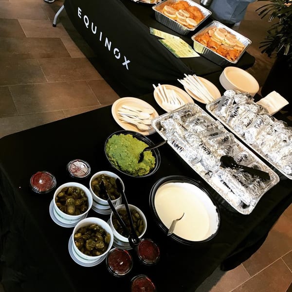 A breakfast buffet with foil-wrapped items, guacamole, jalapeños, and sauces on a black table.