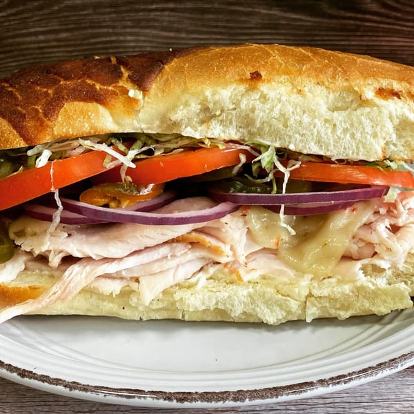 A turkey sub sandwich with melted cheese, lettuce, tomatoes, red onions, and jalapeños.