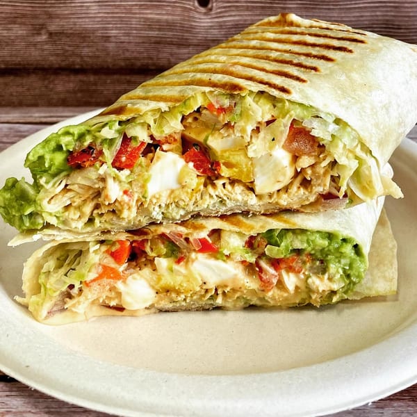 Grilled breakfast burrito, cut in half, filled with eggs, avocado, lettuce, and red peppers.