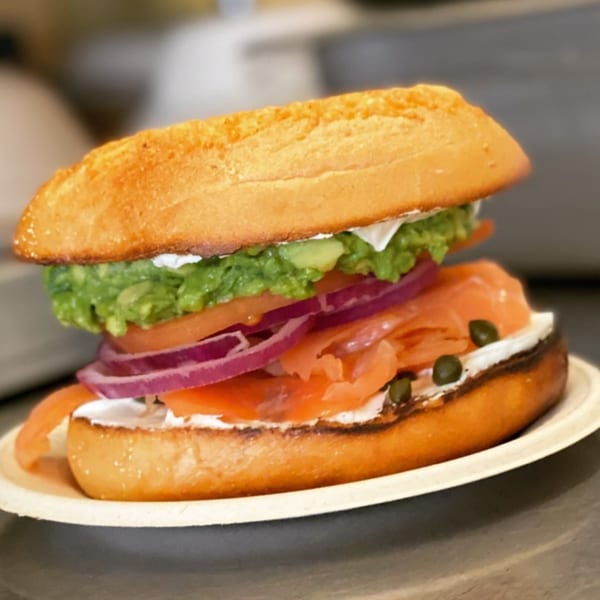 A bagel sandwich with cream cheese, smoked salmon, red onion, tomato, capers, and guacamole.