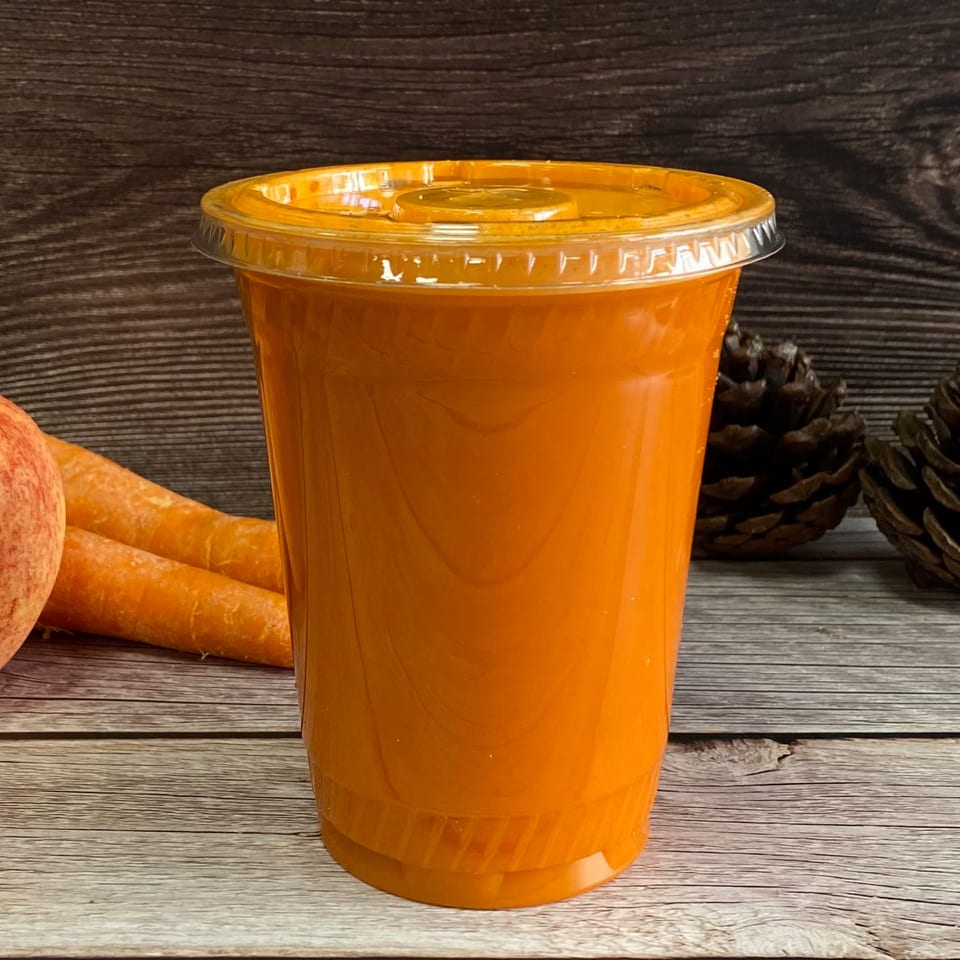 Freshly squeezed orange juice in a clear plastic cup with carrots and pinecones on a wooden table.